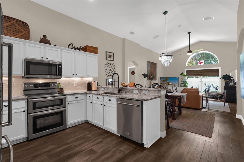 A kitchen with white cabinets, stainless steel appliances, and granite countertops opens to a living area — 1393 WAUKON CIRCLE, CASSELBERRY, FL