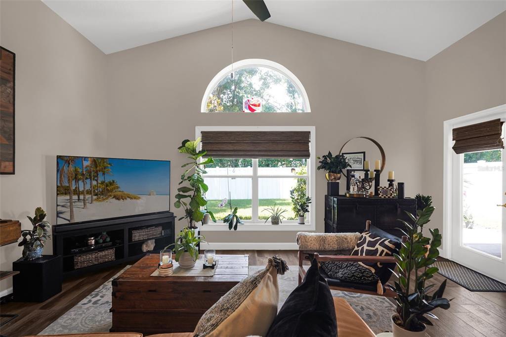 A living room with a vaulted ceiling, arched window, wood flooring, and a television console — 1393 WAUKON CIRCLE, CASSELBERRY, FL