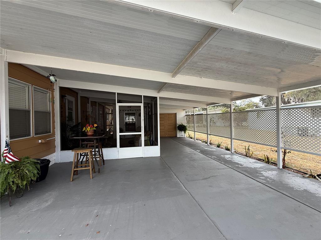 A covered concrete carport extends alongside a screened-in porch with a table and chairs — 50 N BOBWHITE ROAD, WILDWOOD, FL