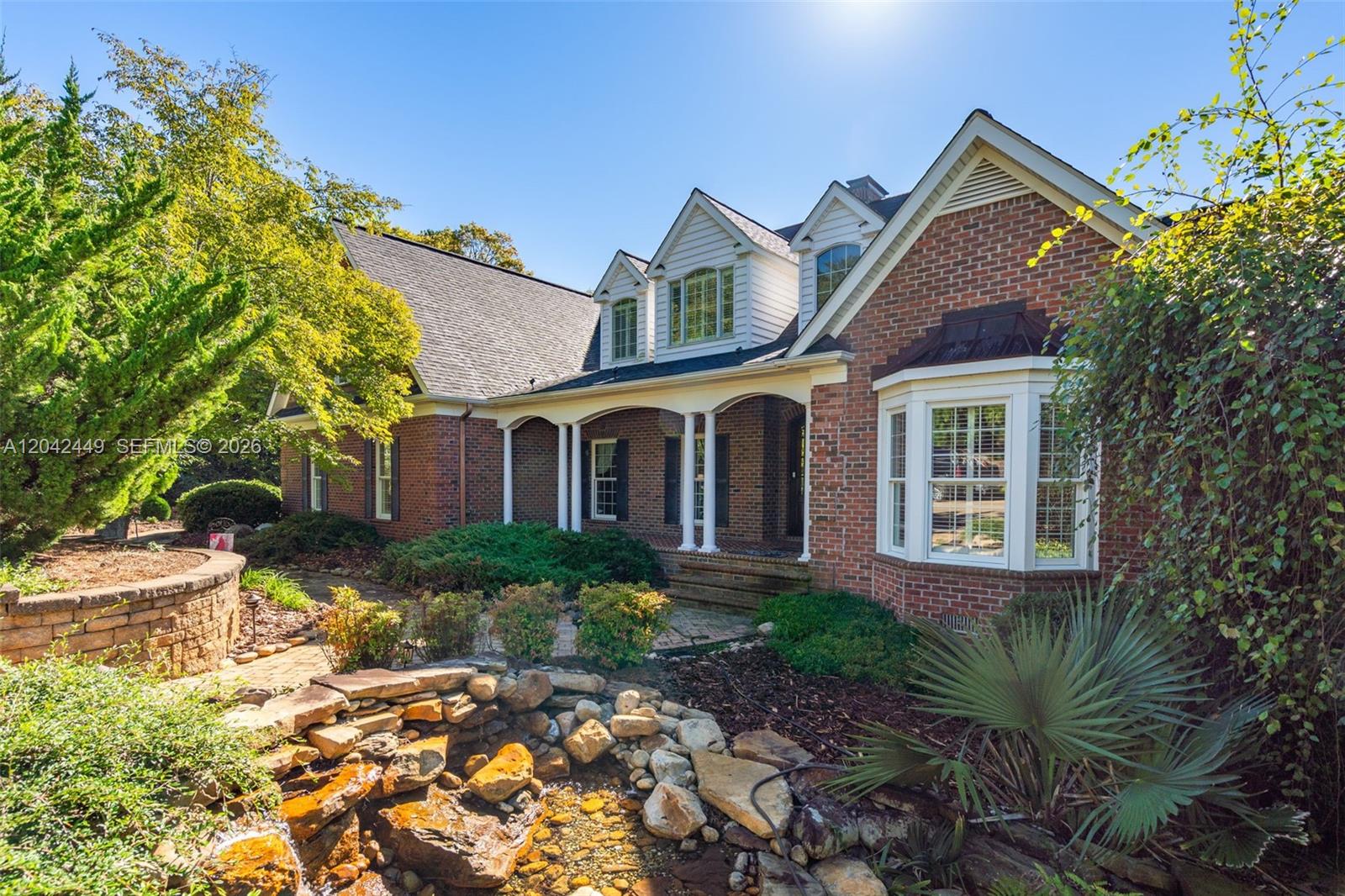 A brick house features a front porch, dormer windows, and a stone-lined water feature — 2579 Grey Rabbit Run, NC 27205, NC