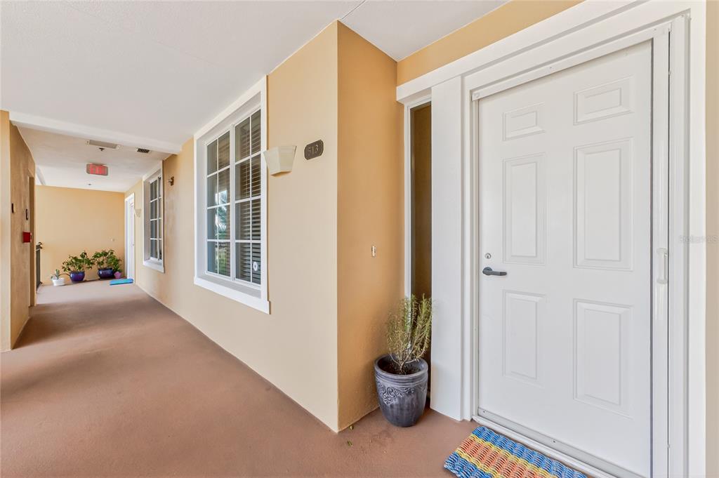 A white front door with a side window sits on a tan outdoor apartment walkway — 167 TAMPA AVENUE E UNIT 513, VENICE, FL