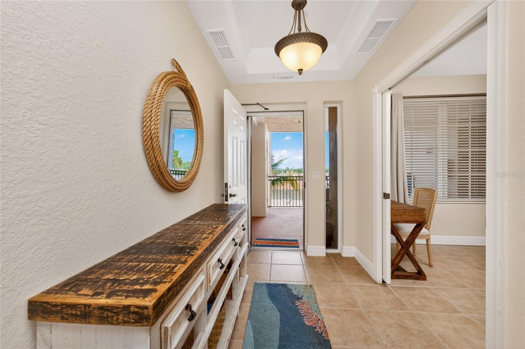 A foyer with a rustic console table, a rope-framed mirror, and a view of a balcony — 167 TAMPA AVENUE E UNIT 513, VENICE, FL