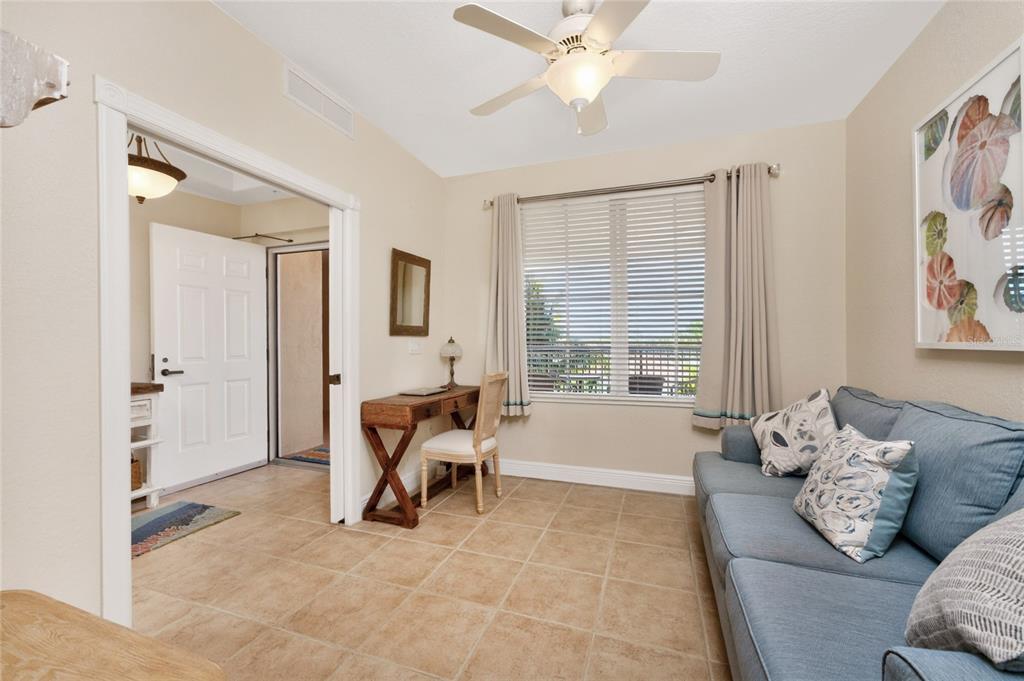 A room with tile floors, a blue sofa, a wooden desk, and a ceiling fan — 167 TAMPA AVENUE E UNIT 513, VENICE, FL