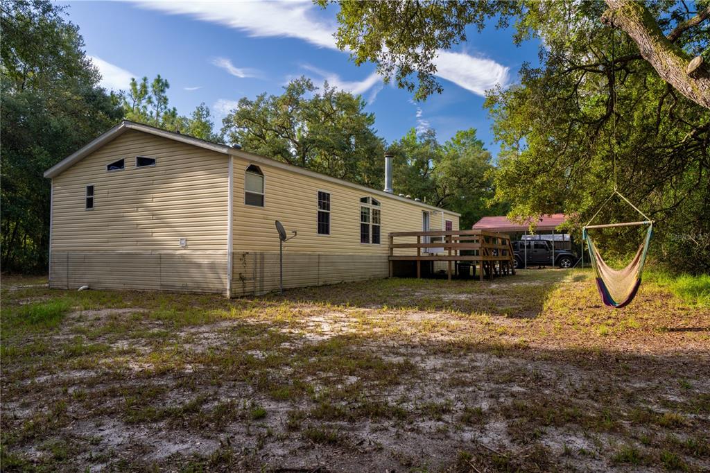 A beige mobile home with a wooden deck and a hammock hanging from a tree — 11934 CR 656H, WEBSTER, FL
