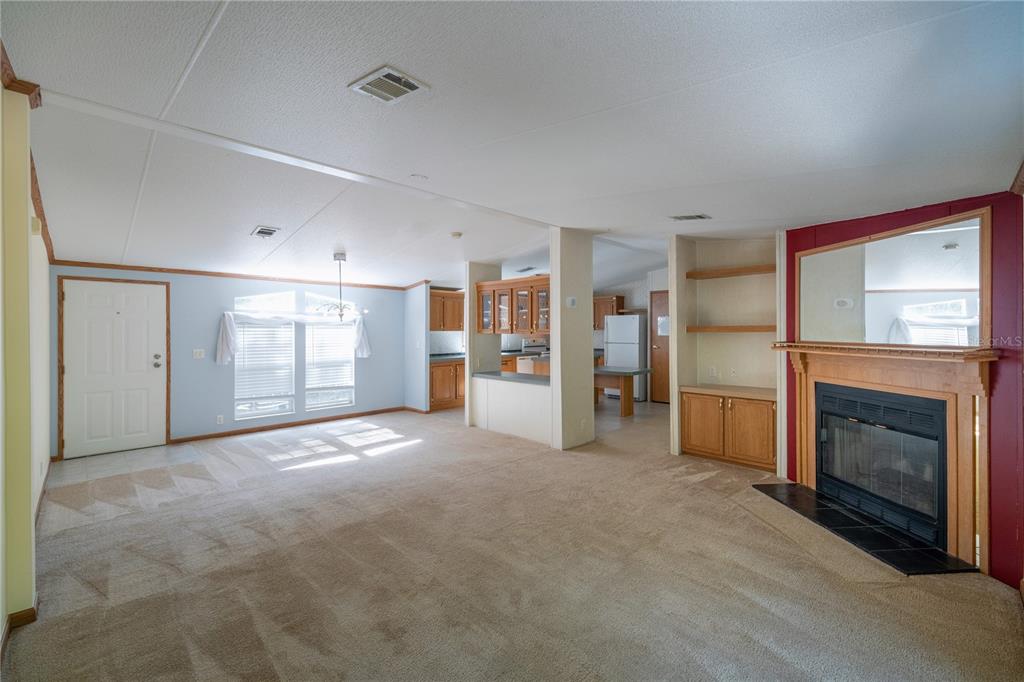 A living room with beige carpet, a fireplace, built-in shelving, and an open kitchen beyond — 11934 CR 656H, WEBSTER, FL