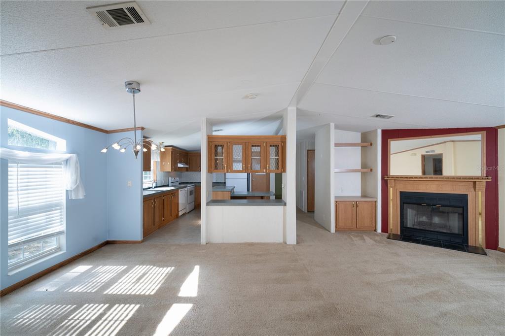 A living room with beige carpet, a fireplace, and an open kitchen with wooden cabinets — 11934 CR 656H, WEBSTER, FL