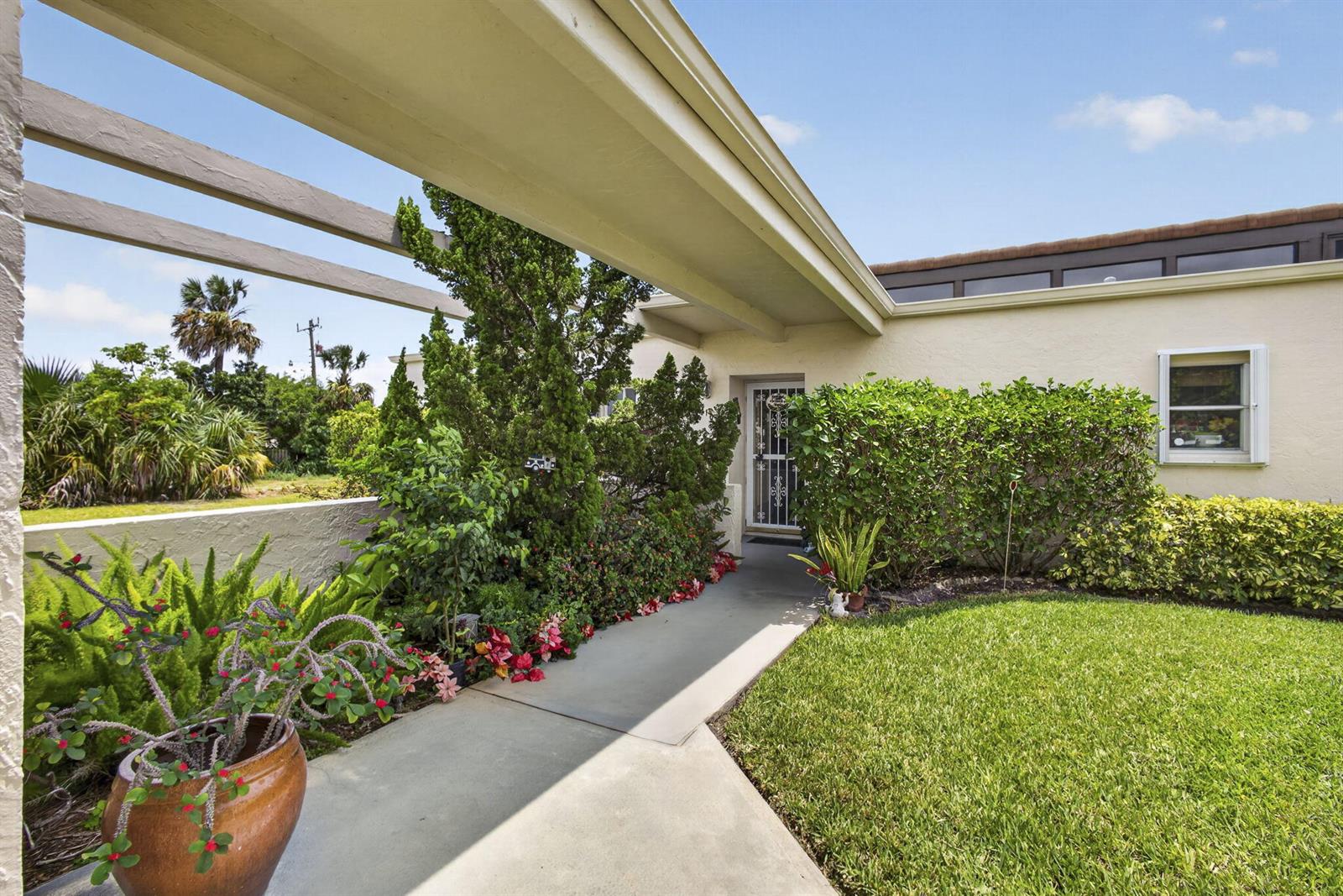 A concrete walkway leads to a front door beneath a pergola-style roof extension — 2651 Boundbrook Boulevard # 110, West Palm Beach FL 33461, WEST PALM BEACH, FL