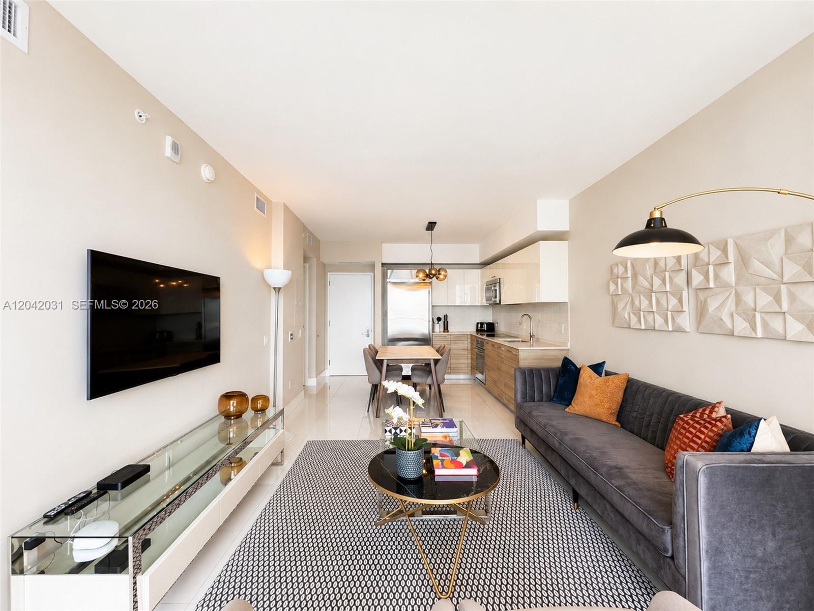 A modern living room and kitchen area features a grey sofa, glass console, and dining table — 1300 Brickell Bay Dr # 2307, Miami FL 33131, MIAMI, FL