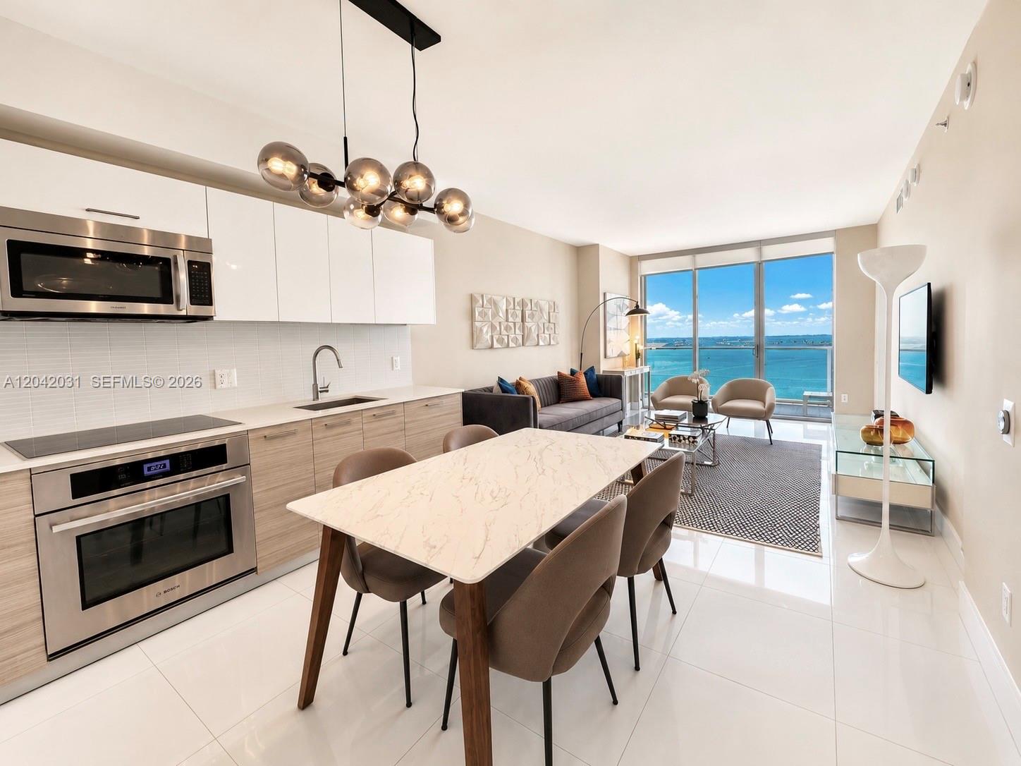 A modern open-concept kitchen and living area features white cabinetry, marble-topped dining, and ocean views — 1300 Brickell Bay Dr # 2307, Miami FL 33131, MIAMI, FL