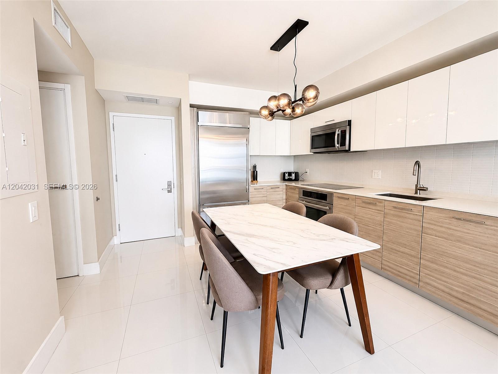 A modern kitchen features white upper cabinets, wood-grain lower cabinets, and a marble-topped dining table — 1300 Brickell Bay Dr # 2307, Miami FL 33131, MIAMI, FL