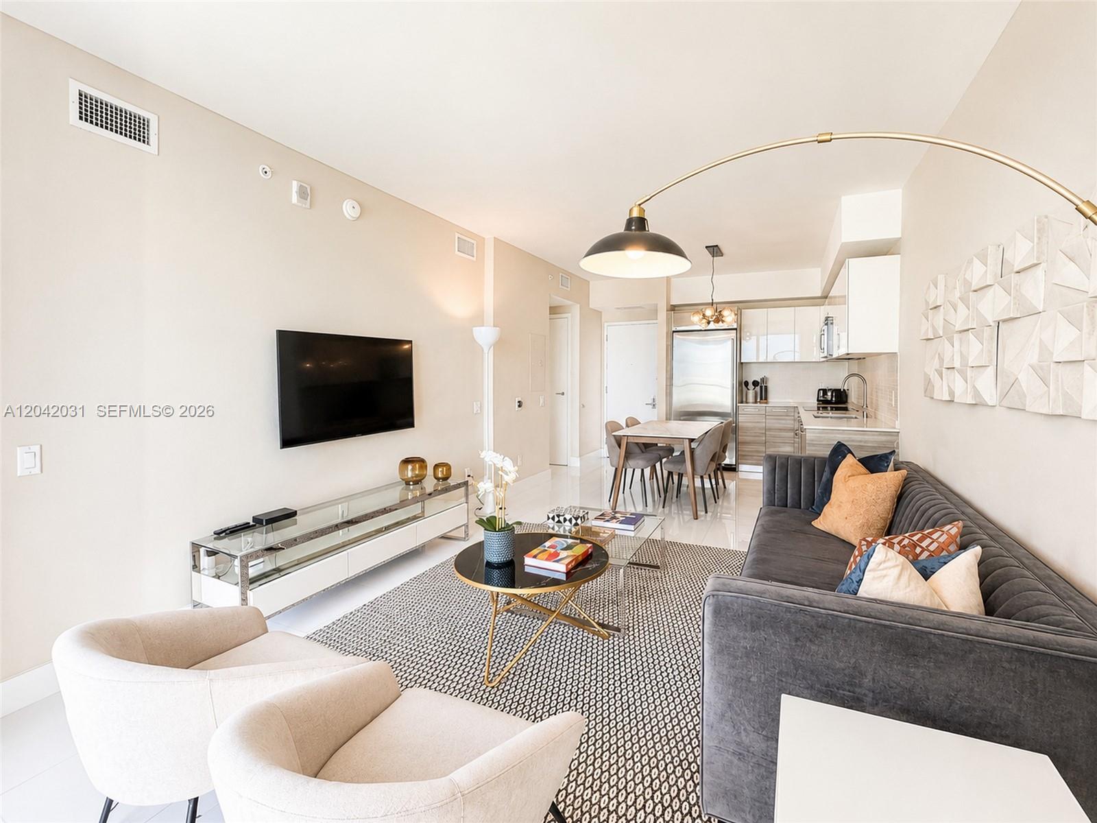 A modern living room features a grey sofa, two beige chairs, and an open kitchen — 1300 Brickell Bay Dr # 2307, Miami FL 33131, MIAMI, FL
