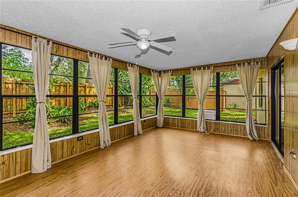 A sunroom with wood-paneled walls, wood-look flooring, large windows, and a ceiling fan — 260 ARBOR GLEN DRIVE, PALM HARBOR, FL