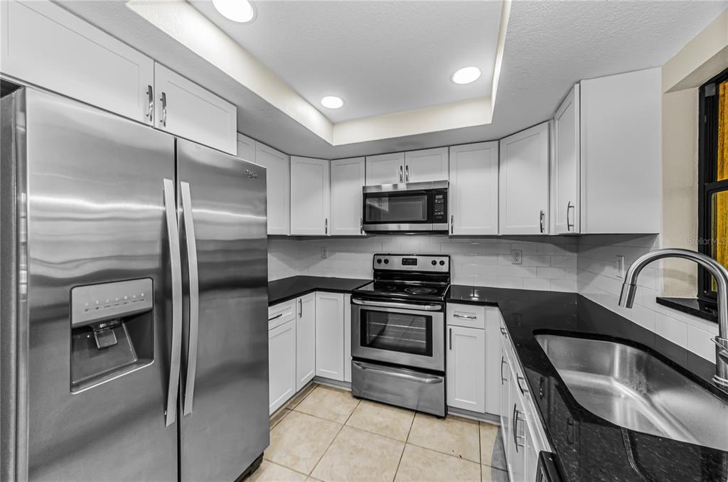A kitchen features white cabinets, black countertops, stainless steel appliances, and a tiled floor — 260 ARBOR GLEN DRIVE, PALM HARBOR, FL