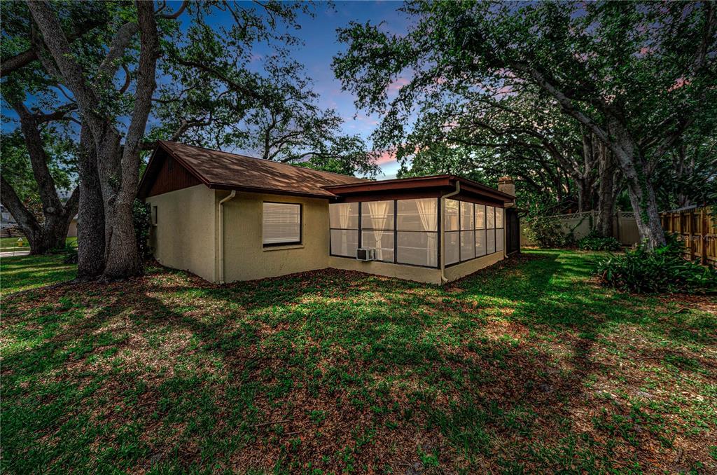 A beige house with a screened-in porch sits in a yard with large oak trees — 260 ARBOR GLEN DRIVE, PALM HARBOR, FL