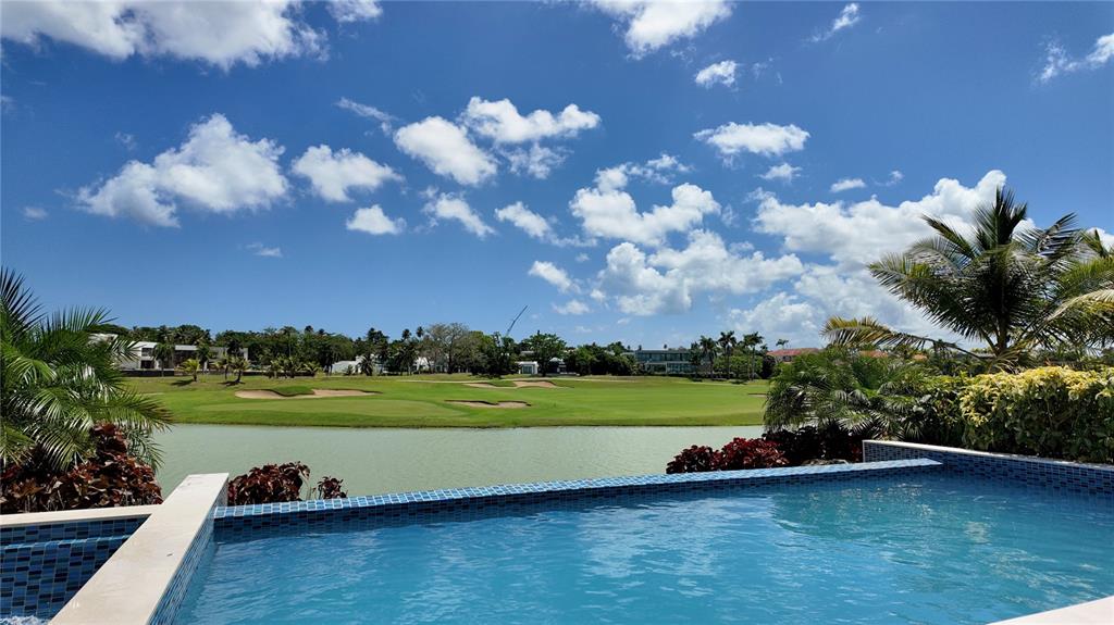 An infinity pool overlooks a pond and a golf course under a blue sky — The Isles, #55 LAKEFRONT HOME,, DORADO, PR