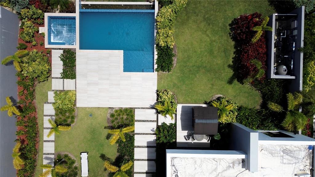 An aerial view shows a backyard with a swimming pool, lawn, landscaping, and paved walkways — The Isles, #55 LAKEFRONT HOME,, DORADO, PR
