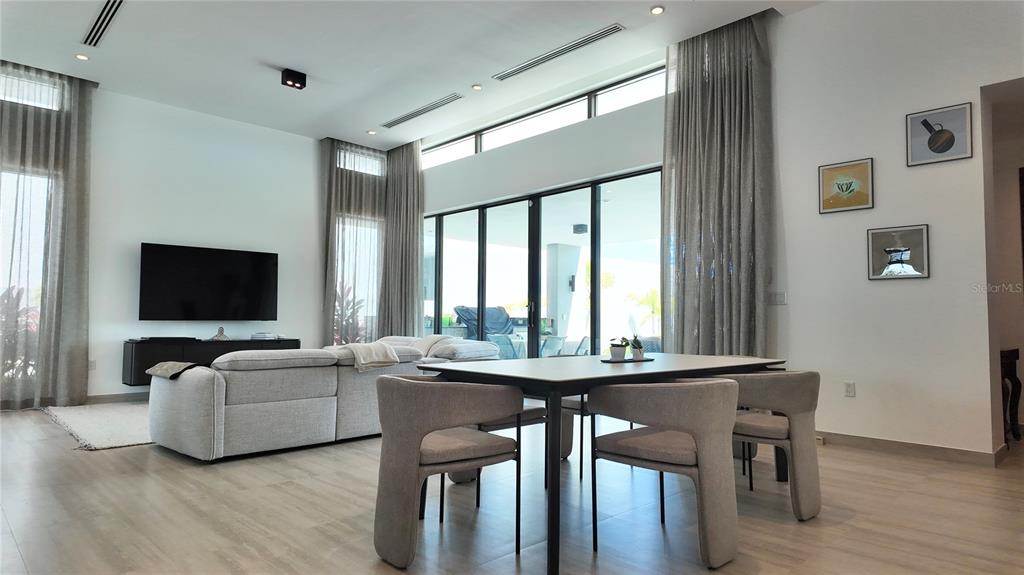 A modern open-concept living and dining area with high ceilings, large windows, and light flooring — The Isles, #55 LAKEFRONT HOME,, DORADO, PR