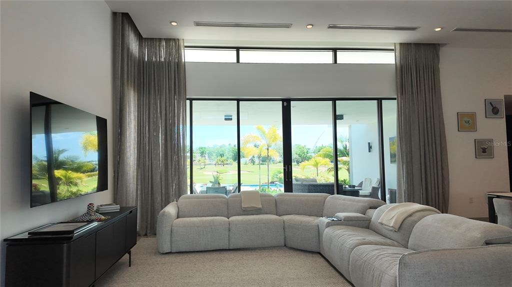 A living room features a large sectional sofa, a wall-mounted television, and floor-to-ceiling windows — The Isles, #55 LAKEFRONT HOME,, DORADO, PR