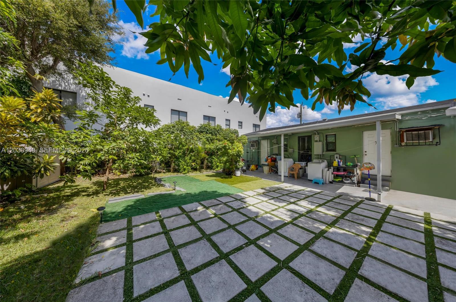 A backyard features a paved patio, patches of artificial turf, and a green exterior wall — MIAMI, FL