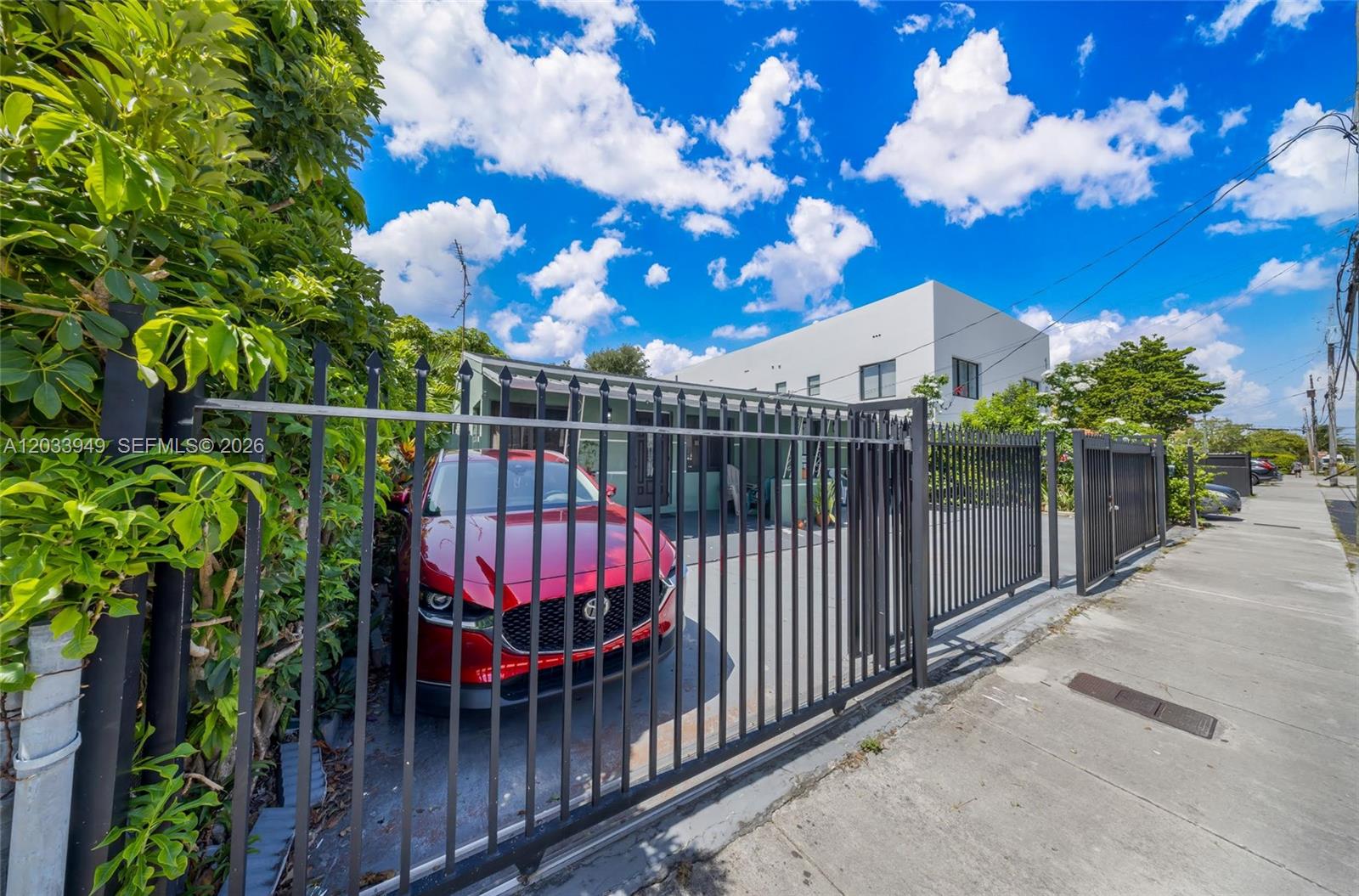 A red car is parked behind a metal fence in front of a house — MIAMI, FL