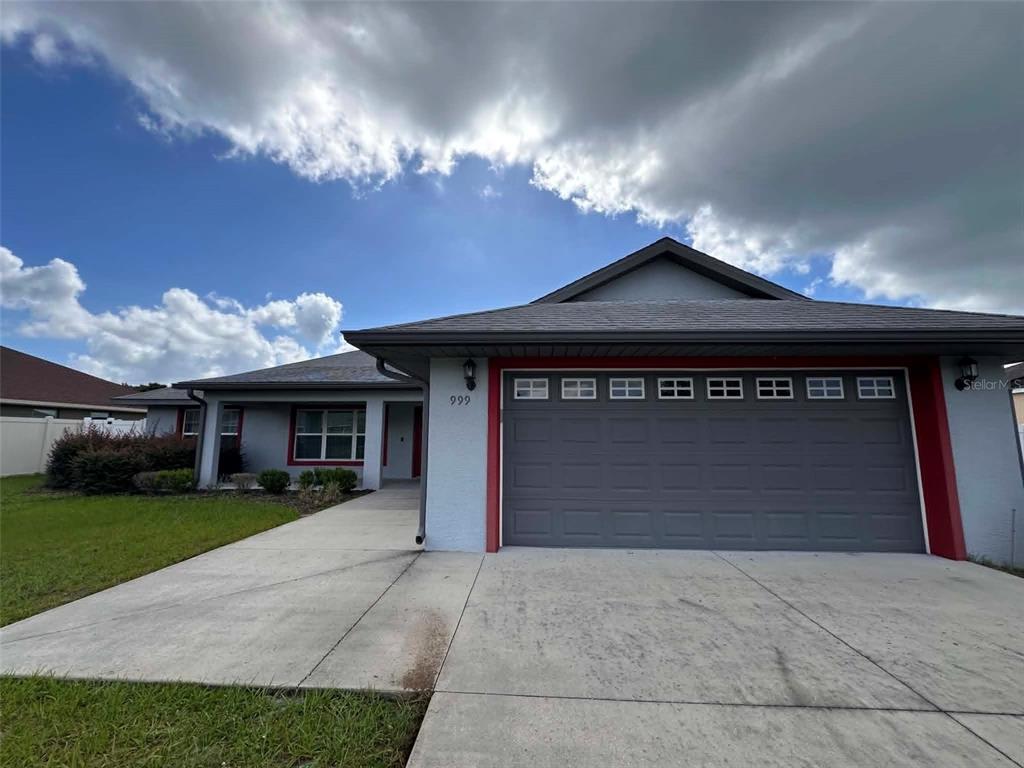 A single-story house with a gray garage, light blue stucco walls, and red trim — 999 SE 69TH AVENUE, OCALA, FL