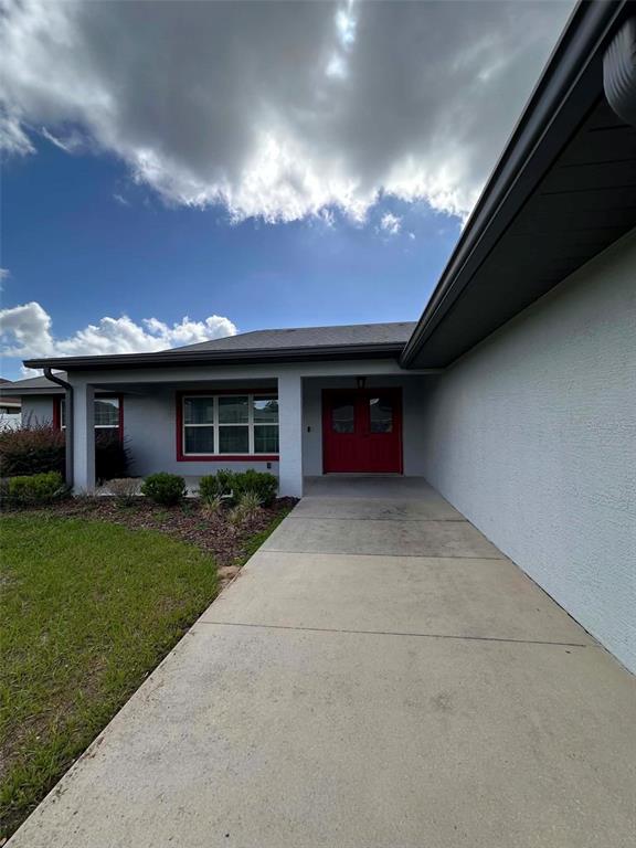 A concrete walkway leads to the red double front doors of a gray stucco house — 999 SE 69TH AVENUE, OCALA, FL