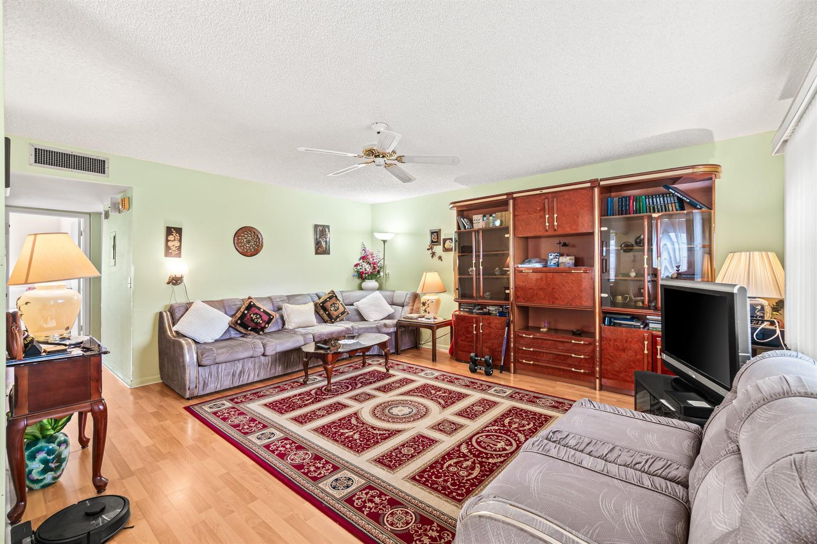 A living room features a large sectional sofa, a red patterned rug, and wooden cabinetry — 508 Normandy K # 508, Delray Beach FL 33484, DELRAY BEACH, FL