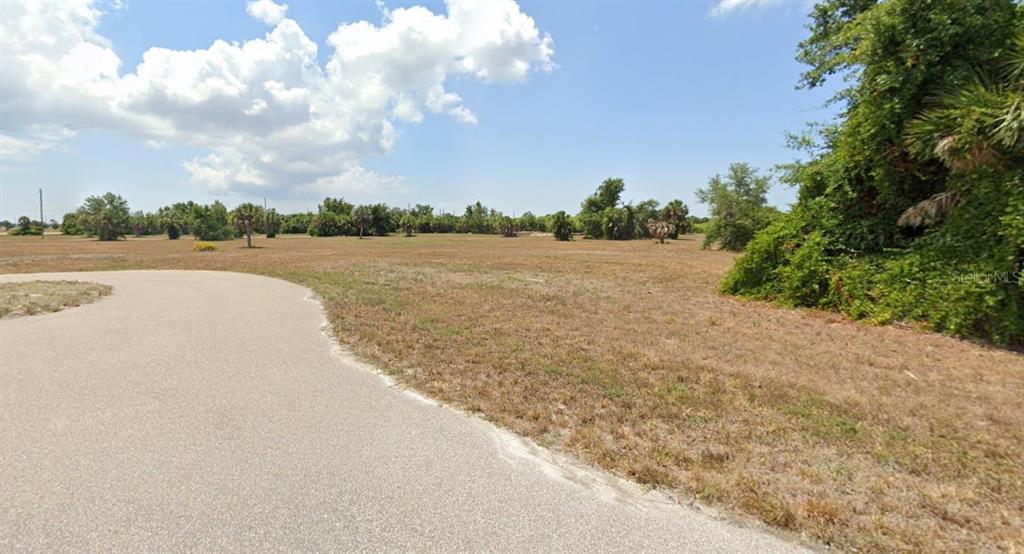 A paved road curves alongside a large, flat, grassy vacant lot with scattered trees — 21 HULL COURT, PLACIDA, FL