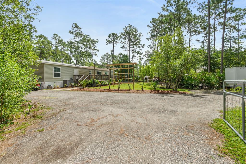 A gravel driveway leads to a mobile home with a wooden deck and garden trellis — 2553 GREENTREE STREET, BUNNELL, FL