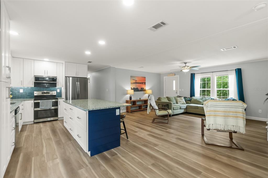 An open-concept kitchen with a blue island and stainless appliances flows into a living area — 2553 GREENTREE STREET, BUNNELL, FL
