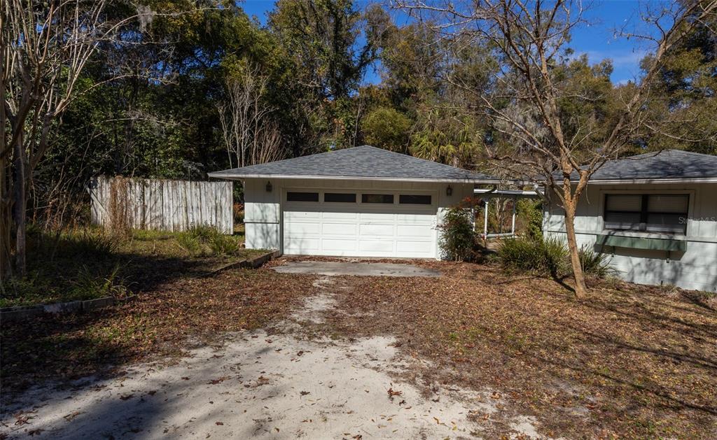 A detached white garage with a gray shingled roof sits on a leaf-covered dirt lot — 6116 TROUT STREET, MELROSE, FL