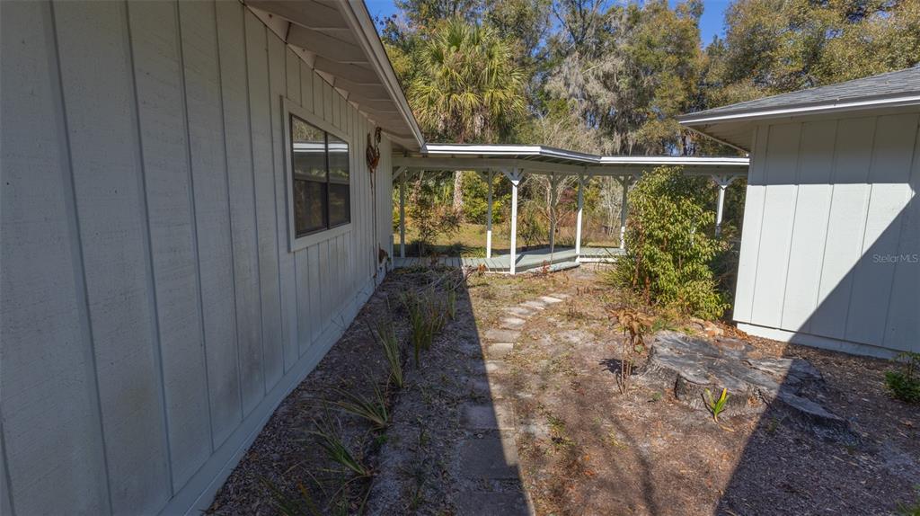 A covered walkway connects two light-colored buildings with vertical siding over a dirt yard — 6116 TROUT STREET, MELROSE, FL