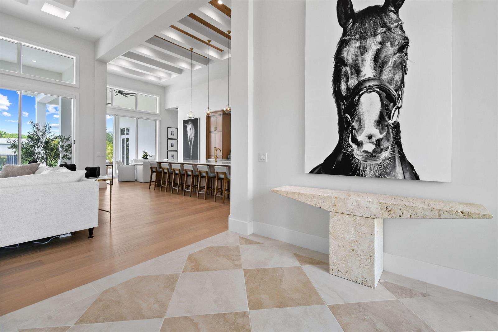 A bright, open-concept living area features a stone console table, horse artwork, and wood beams — 9105 Whippoorwill Trail, Jupiter FL 33478, JUPITER, FL