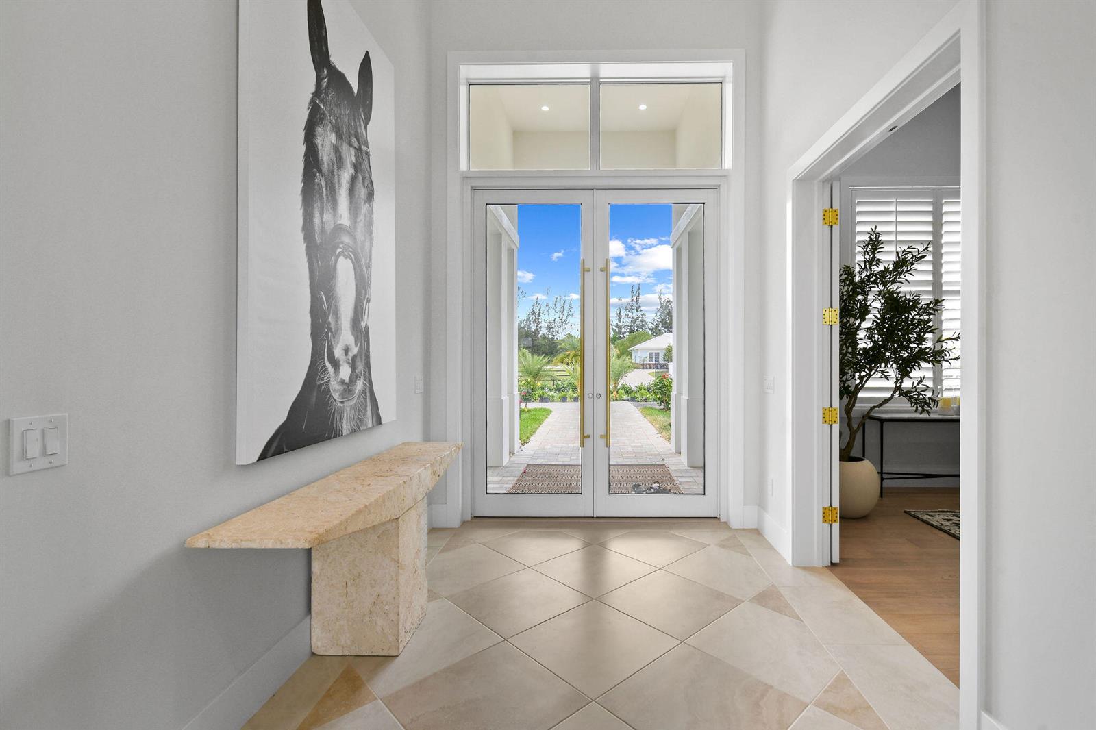 A bright entryway features a stone console table, horse artwork, and glass double doors — 9105 Whippoorwill Trail, Jupiter FL 33478, JUPITER, FL