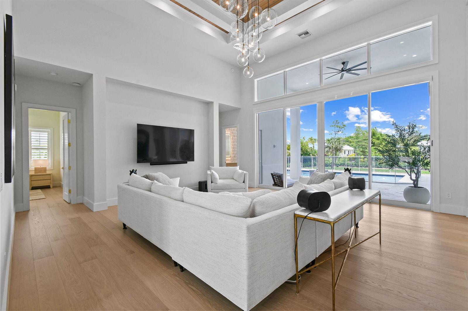 A bright living room features a white sectional, high tray ceiling, and large sliding glass doors — 9105 Whippoorwill Trail, Jupiter FL 33478, JUPITER, FL