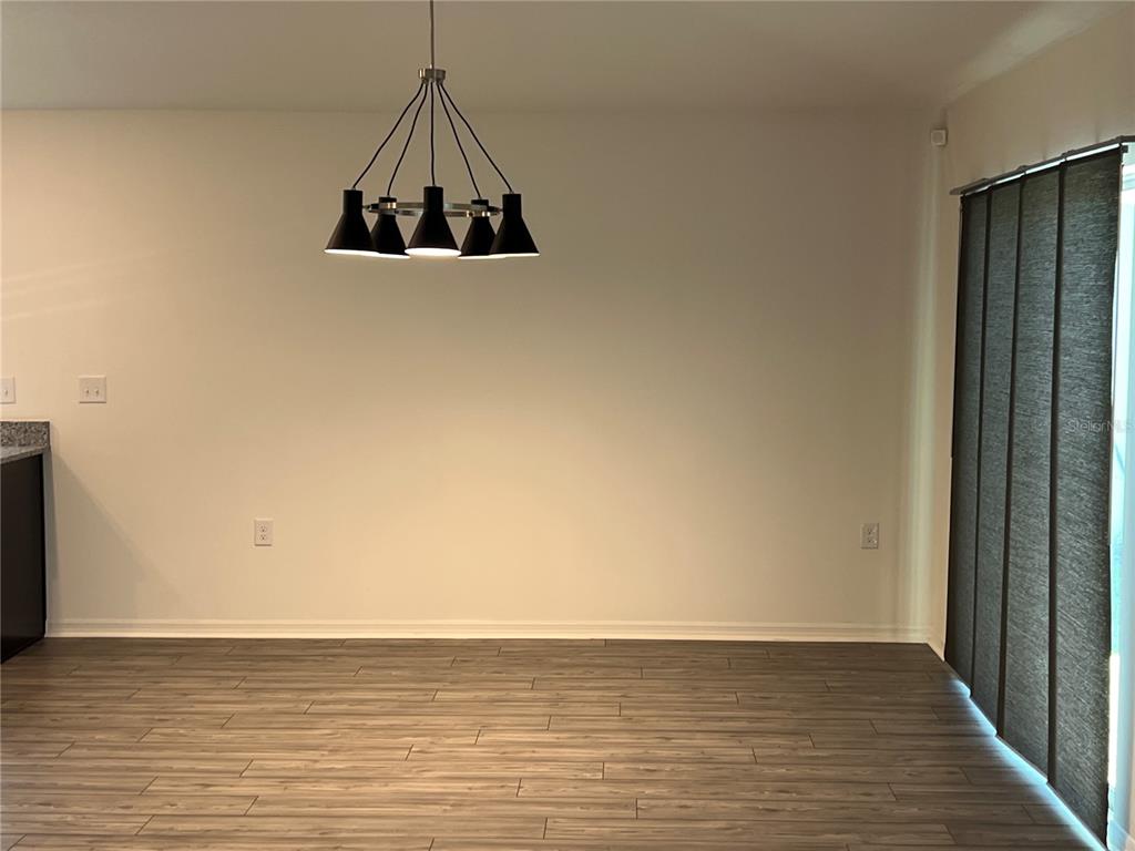 A dining area features wood-look flooring, a modern black chandelier, and sliding glass patio doors — 3838 WHITETAIL COURT, ST CLOUD, FL