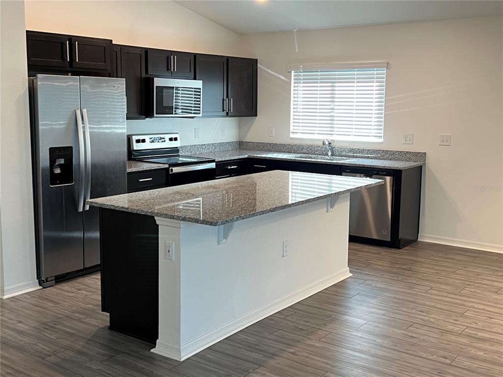 A kitchen features dark cabinets, granite countertops, stainless steel appliances, and a central island — 3838 WHITETAIL COURT, ST CLOUD, FL