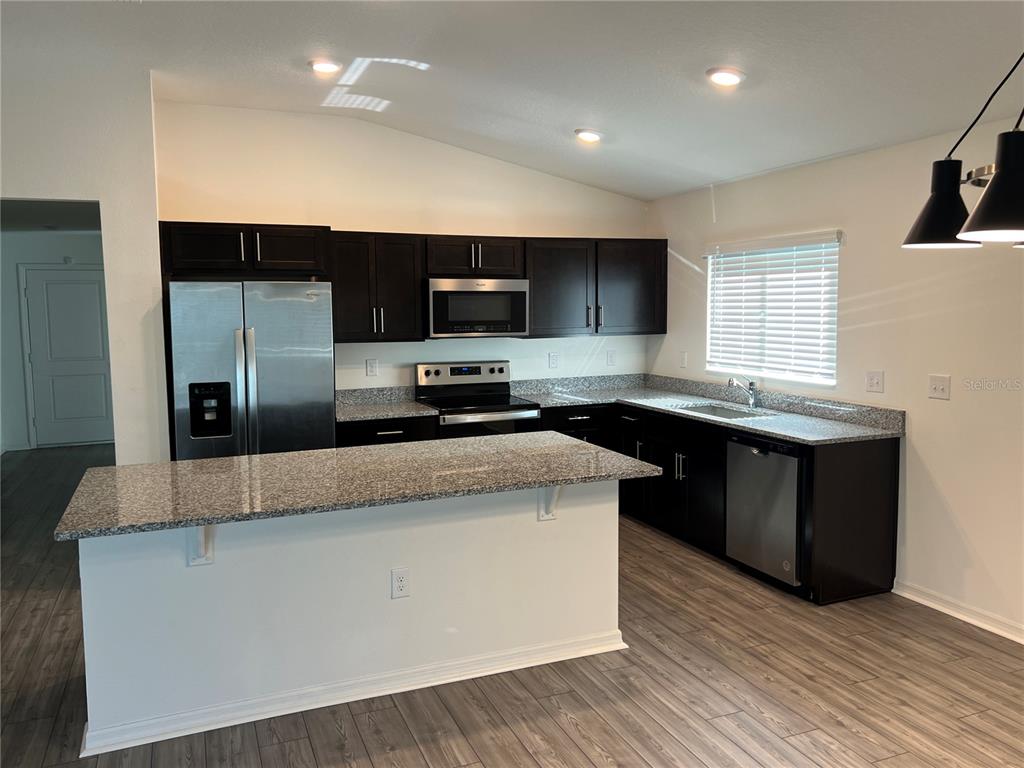 A modern kitchen features dark cabinetry, granite countertops, stainless steel appliances, and a center island — 3838 WHITETAIL COURT, ST CLOUD, FL