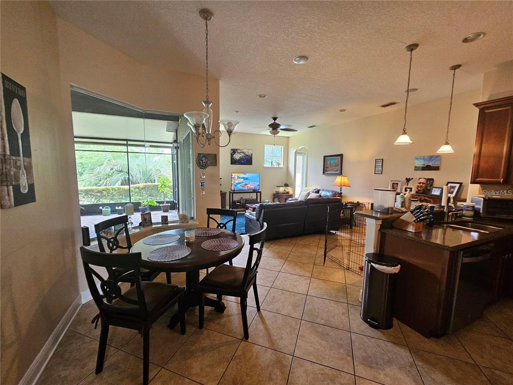 An open-concept kitchen and dining area features tile flooring, dark cabinetry, and a screened patio — 6178 HEDGESPARROWS LANE, SANFORD, FL
