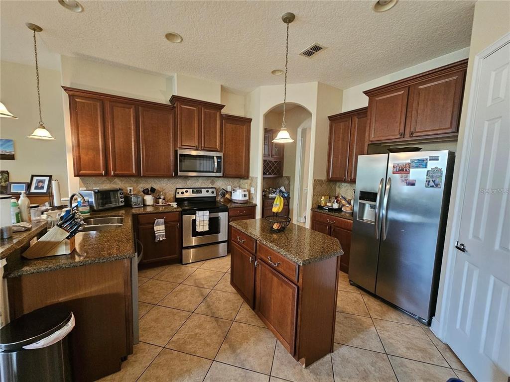 A kitchen features dark wood cabinets, granite countertops, a center island, and stainless steel appliances — 6178 HEDGESPARROWS LANE, SANFORD, FL