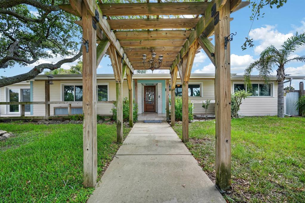 A wooden pergola covers a concrete walkway leading to the front entrance of a house — 2071 S PENINSULA DRIVE, DAYTONA BEACH, FL