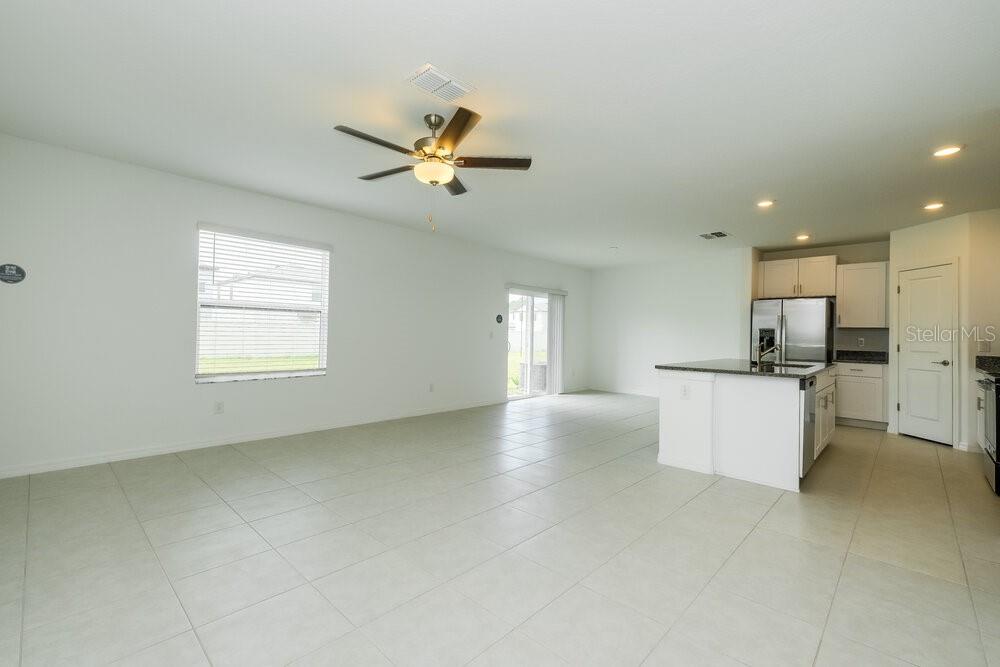 An open-concept living area features light tile flooring, a ceiling fan, and a kitchen island — 17854 BEAMING RAYS LANE, LUTZ, FL