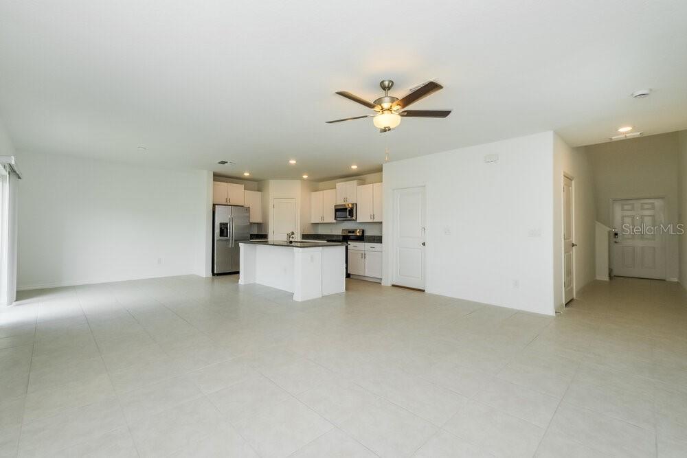 An open-concept kitchen with white cabinets and a center island overlooks a large tiled room — 17854 BEAMING RAYS LANE, LUTZ, FL