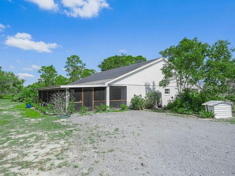 A gravel driveway leads to a house with a large screened-in porch and white siding — 1850 S LAKE REEDY BOULEVARD, FROSTPROOF, FL