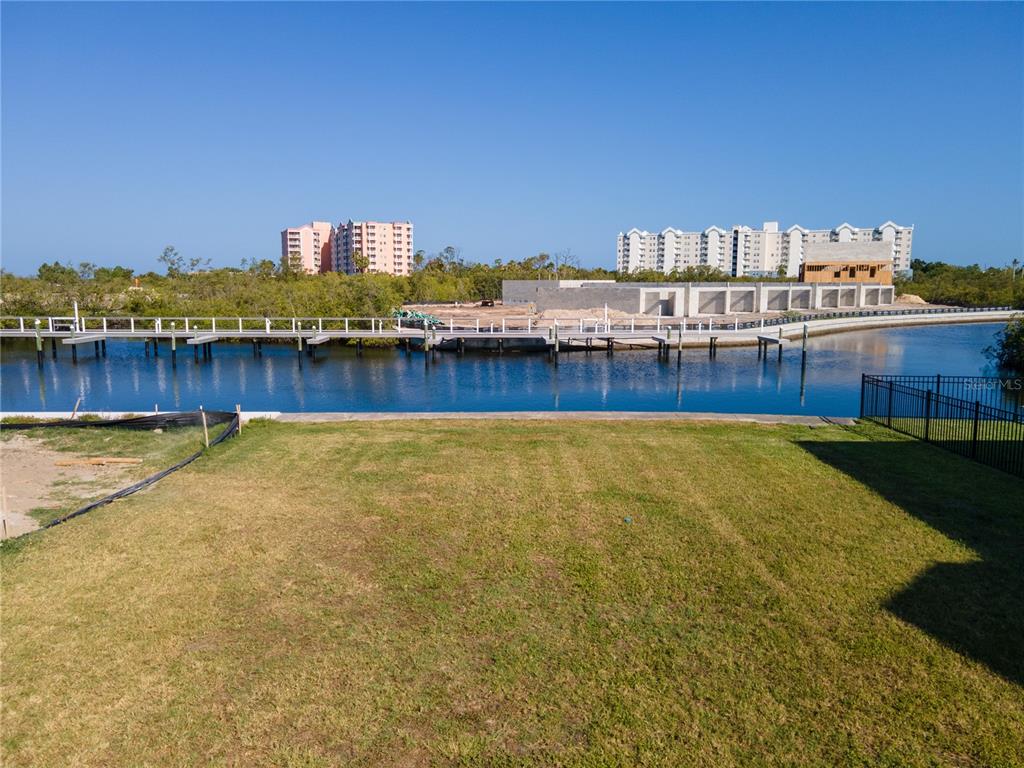 A grassy backyard overlooks a canal with a wooden dock and distant apartment buildings — Lot 7 ELISABETHAN LANE, NEW PORT RICHEY, FL