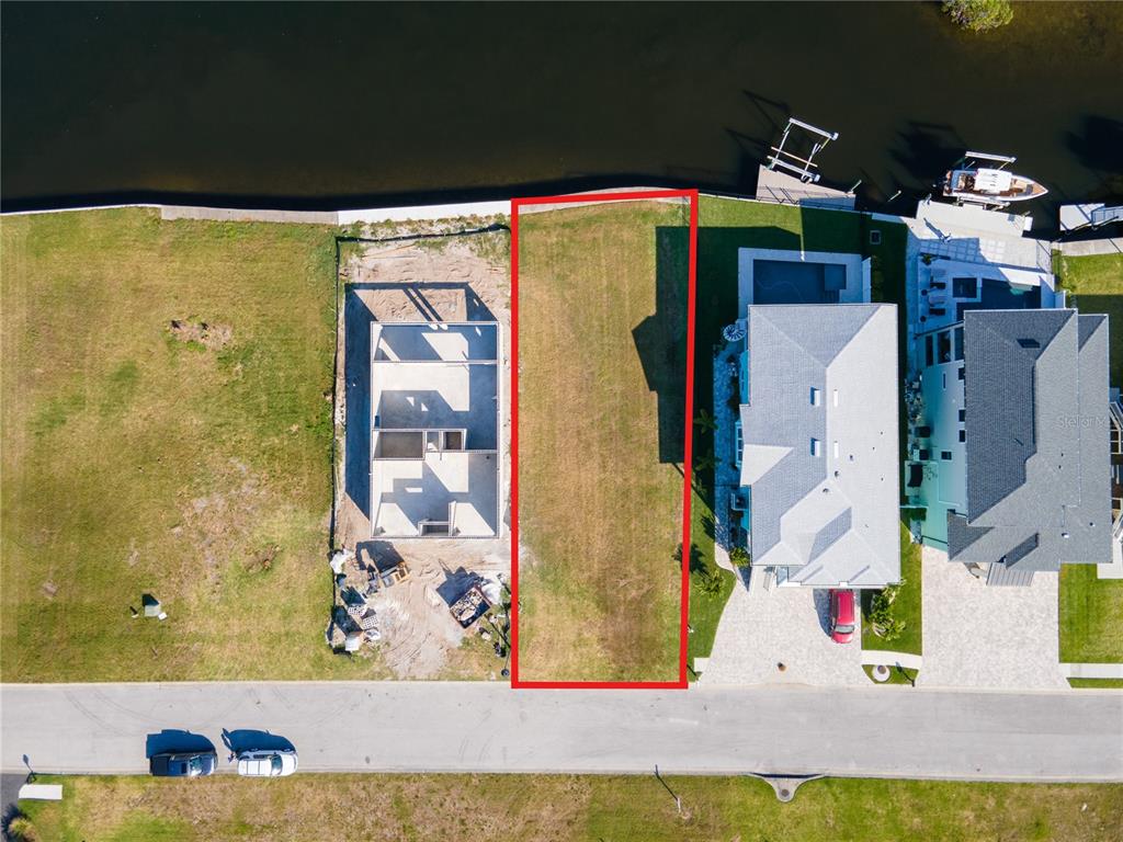 An aerial view shows a vacant, rectangular waterfront lot outlined in red between two houses — Lot 7 ELISABETHAN LANE, NEW PORT RICHEY, FL