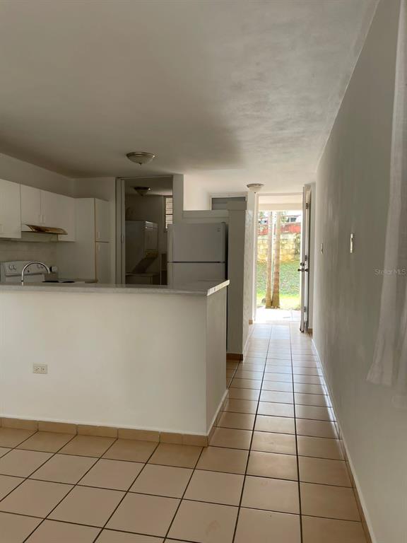 A kitchen with white cabinets and a breakfast bar opens to a tiled hallway outdoors — 1802 BOULEVARD DE LA MEDIA LUNA UNIT 1802, CAROLINA, PR