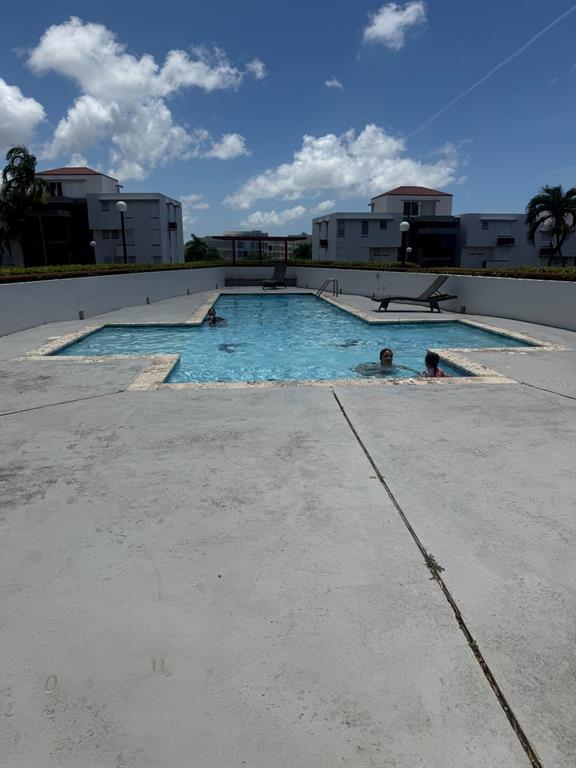A cross-shaped outdoor swimming pool is surrounded by a concrete deck and apartment buildings — 1802 BOULEVARD DE LA MEDIA LUNA UNIT 1802, CAROLINA, PR