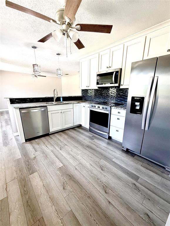 A kitchen features white cabinets, stainless steel appliances, a black backsplash, and wood-look flooring — 1088 NOMAD ROAD, PUNTA GORDA, FL