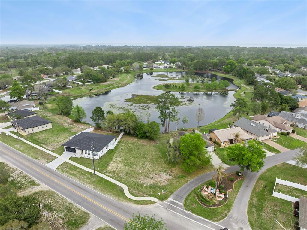 An aerial view shows a suburban neighborhood with houses surrounding a large central pond — COUNTY ROAD 473, LEESBURG, FL